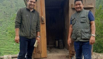 Two men standing in front of a small hut.