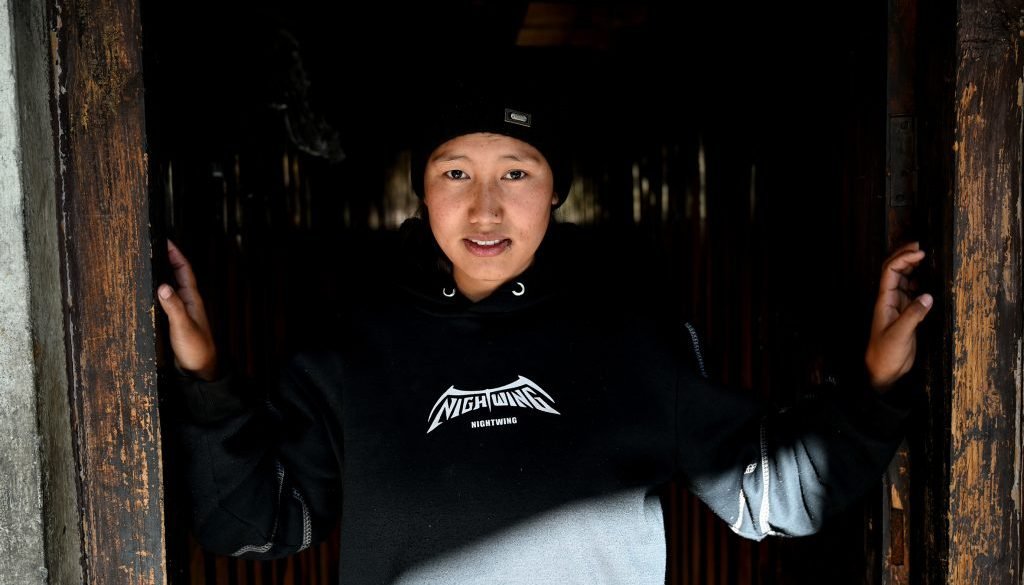 Young woman standing in door frame, dressed in black hoody and black hat